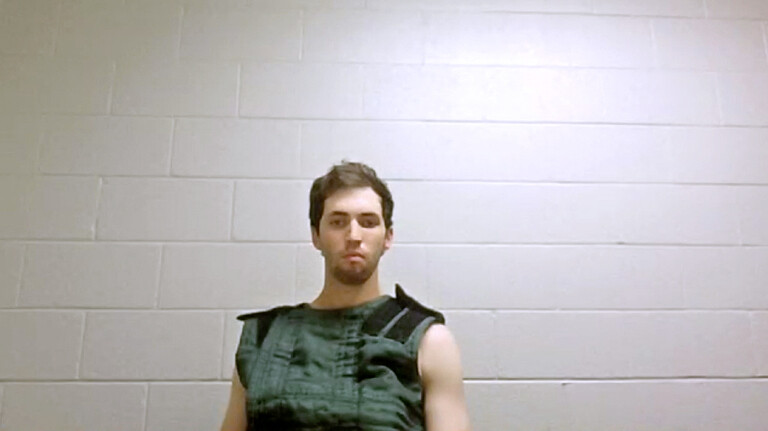 Tyler Robinson sitzt vor einer weißen gemauerten Wand. Sein Blick geht in die Leere.