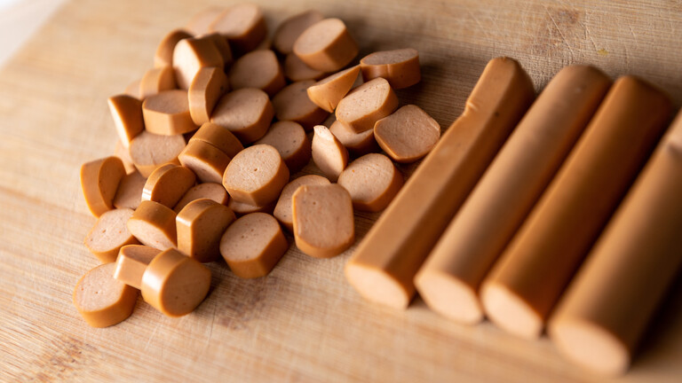 Vegetarische Würstchen liegen geschnitten und halbiert auf einem Schneidebrett in einer Küche.