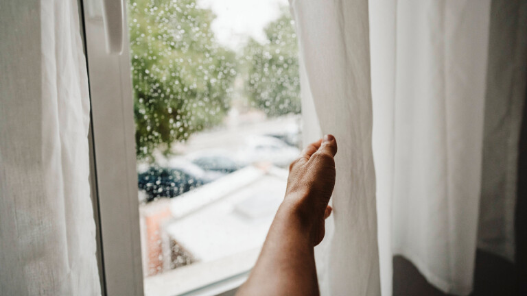 Die Hand einer Frau schiebt einen Vorhang beiseite.