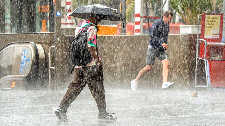 Foto: Münchner flüchten vor dem Wolkenbruch am Stachus, nur ein Münchner durchquert ruhig das Unwetter mit seinem Regenschirm, München, Juli 2025 Deutschland