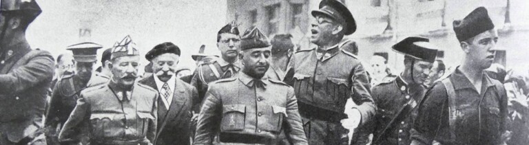 Schwarz-Weiß-Fotografie aus dem August 1936: General Francisco Franco schreitet in Burgos flankiert von den Generälen Emilio Mola, Miguel Cabanellas und José Cavalcanti durch eine Straße.