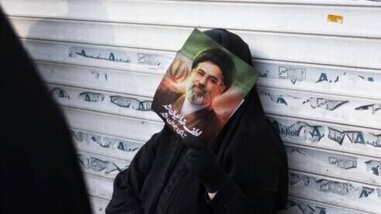 Eine verschleierte Iranerin lehnt sich während einer Jubeldemonstration für Mojtaba Khamenei Anfang März 2026 an die Jalousie eines Geschäfts.