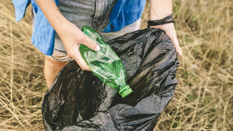 Eine Frau sammelt im Freien Plastikmüll aus hohem Gras.