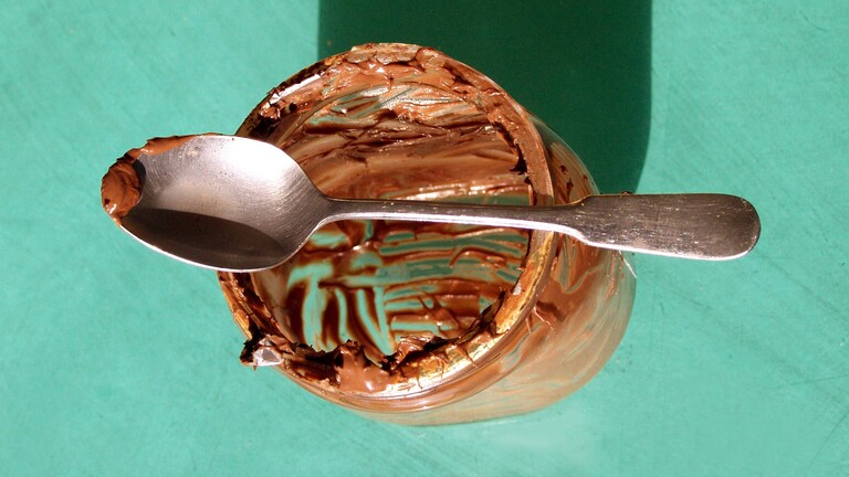 Leer gekratzes Nuss-Nougat-Glas auf dem ein Löffel mit der Creme liegt