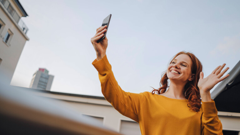 Eine Frau lächelt und winkt in ihr Smartphone.