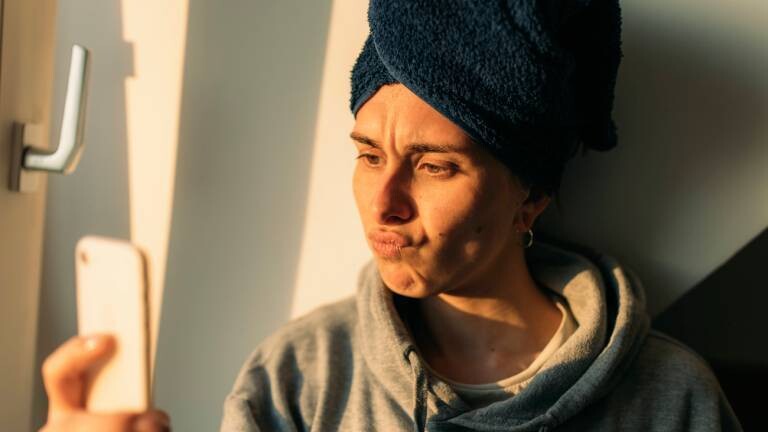 Frau mit Handtuchturban schaut frustriert aufs Smartphone.