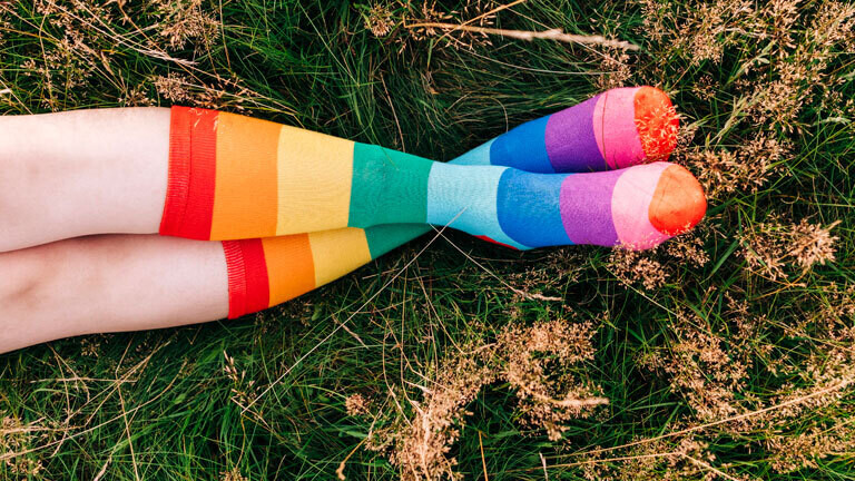 Eine Frau liegt auf einer Wiese und trägt Regenbogensocken