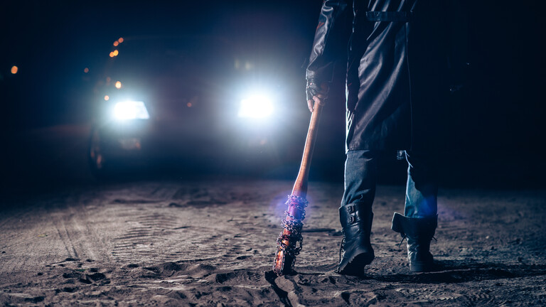 Nahaufnahme der Hand eines Serienmörders mit einem blutigen Baseballschläger, im Hintergrund Scheinwerferlicht eines Autos bei Nacht