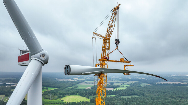 Ein mobiler Kran hebt ein Rotorblatt zum Maschinenhaus einer Windenergieanlage. (Windpark Große Heide in Dorsten,17.08.2023)
