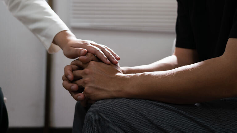 Ärztin legt bestärkend die Hand auf die Hand eines Patienten.