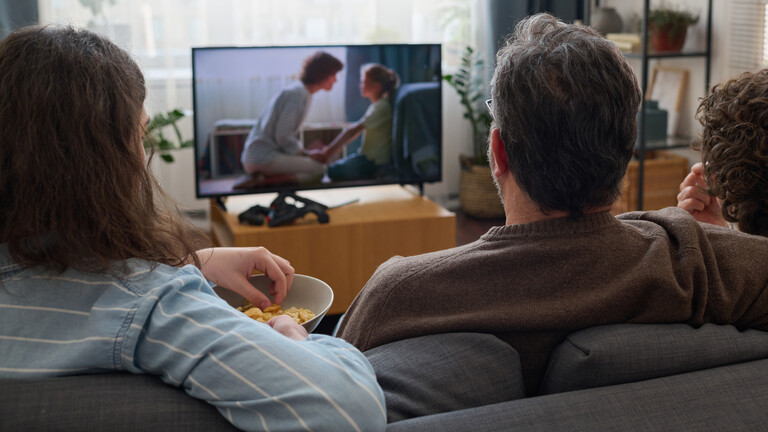 Eine Familie sitzt auf der Couch und guckt gemeinsam Fernsehen.