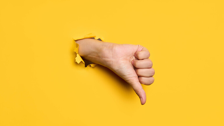 Hand mit Daumen runter greift durch eine Papierwand