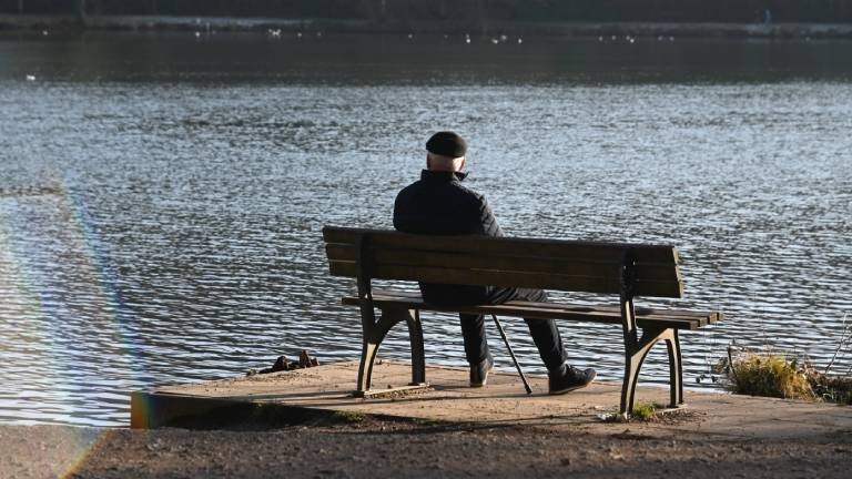 Ein älterer Mann sitzt auf einer Bank und blickt auf einen See