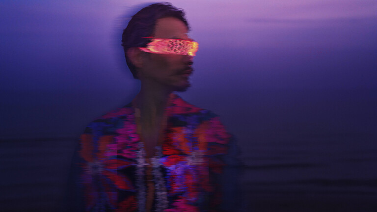 Ein Mann trägt eine pink-orange leuchtende schmale VR-Brille. Er befindet sich draußen. Es scheint, als gehe es von der Dämmerung in die Nacht über. Das Bild ist leicht verschwommen.
