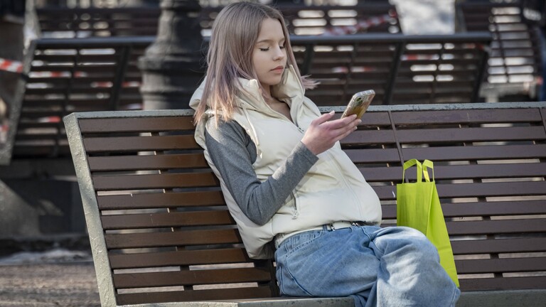 Eine junge Frau sitzt mit ihrem Smartphone auf einer Parkbank