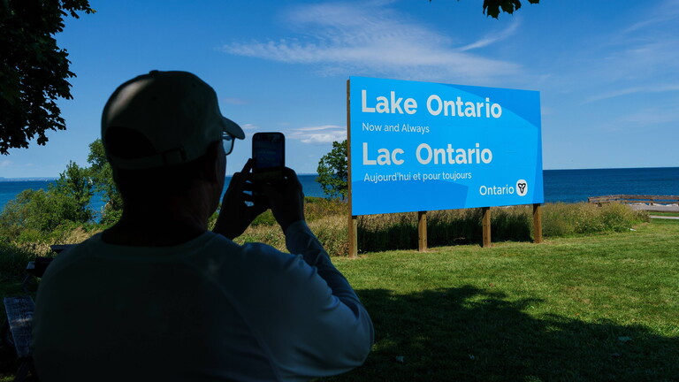 Foto einer Person von hinten, die am Samstag, dem 29. August 2026, das neue Schild für den Ontariosee im Fifty Point Conservation Area in Grimsby, Ontario fotografiert