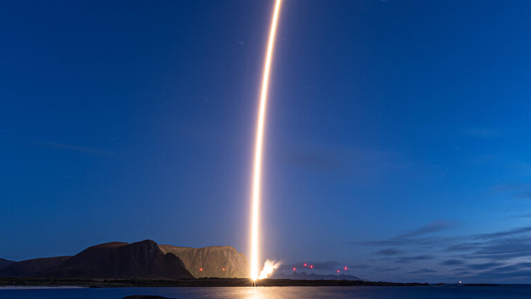 Start der Trägerrakete "Spectrum" des deutschen Unternehmens Isar Aerospace am 5. September 2026 vom Weltraumbahnhof Andøya in Norwegen: Ein Lichtbogen zieht sich von der felsigen Küste in den dunkelblauen Himmel.