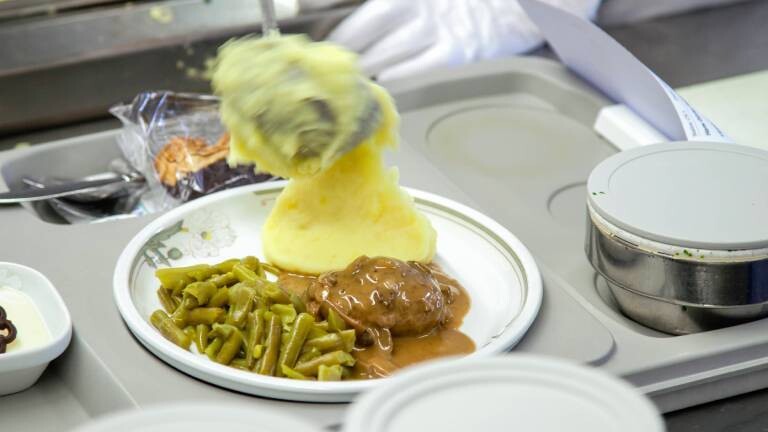 Kartoffelbrei wird mit Kelle auf Teller mit Bohnen und Soße geklatscht