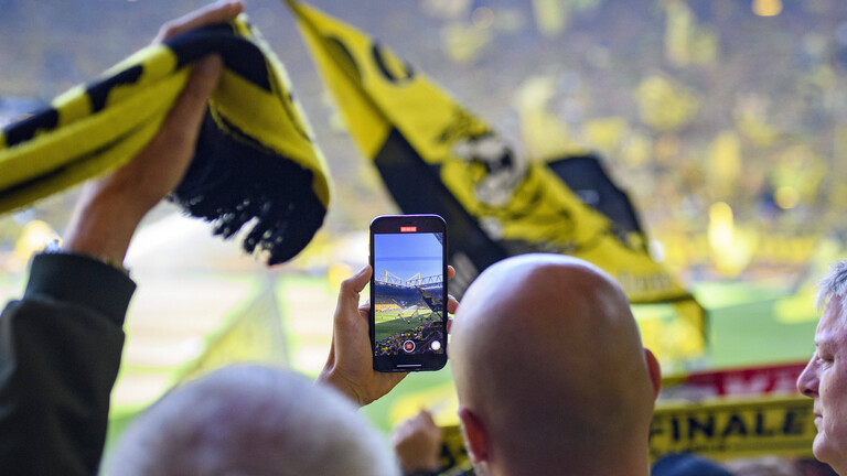 Ein BVB-Fan auf der Tribüne beobachtet den Spielverlauf über sein Handy-Display.