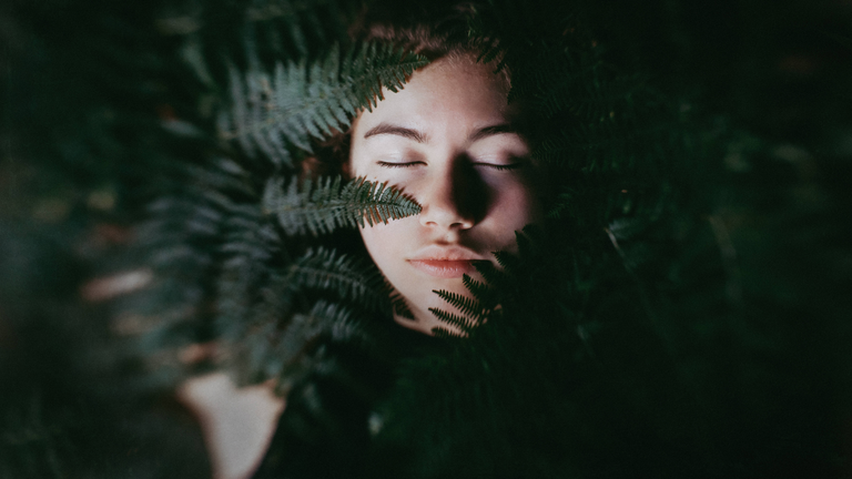 Das Gesicht eines jungen Menschen im Vordergrund ein Farn