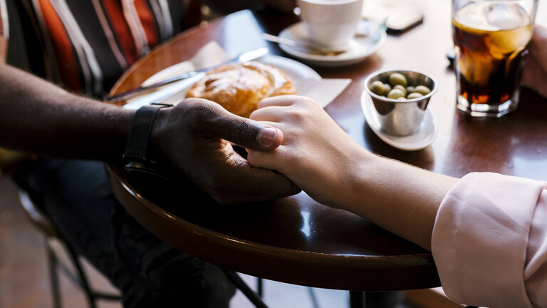Nahaufnahme der Arme und Hände eines Pärchens, die im Café auf dem Tisch Händchen halten