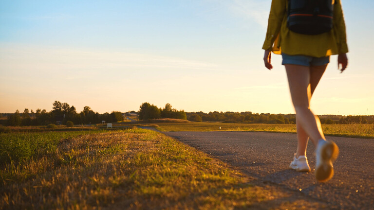 Frau mit Rucksack geht entlang der Straße in den Sonnenuntergang.