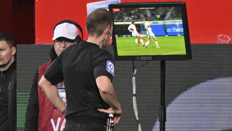 Ein Schiedsrichter checkt bei einem Fußballmatch ein Video                                                                                         Ein Schiedsrichter checkt bei einem Fußballspiel ein Video, das ihm vom VAR Vido-Assistenten bereitgestellt wurde.