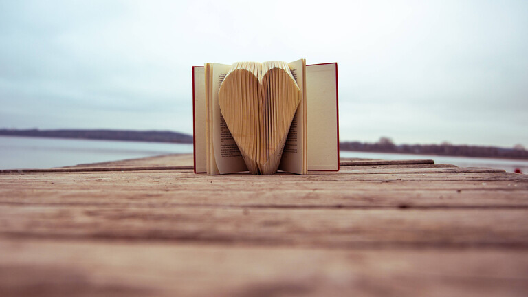 Paperart: Die Seiten eines Buches, das auf dem Steg an einem See liegt, wurden zu einem Herz geformt