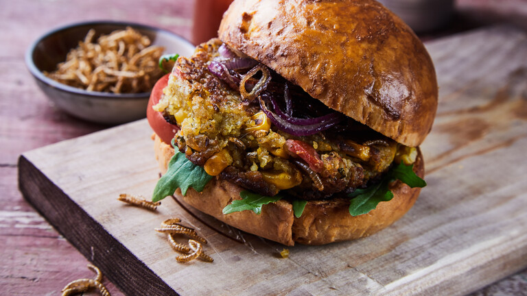 Ein Burger mit frittierten Mehlwürmern, angerichtet auf einem Holzbrettchen.