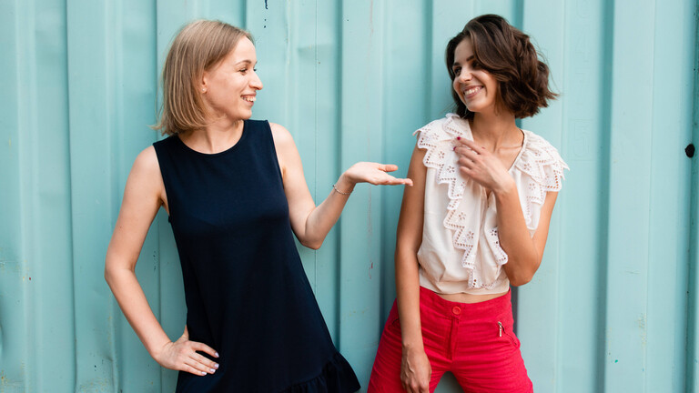 Zwei Frauen, die eine reicht der anderen die Hand. Die andere ziert sich etwas.