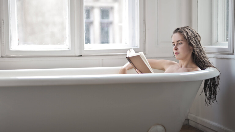 Eine Frau mit Buch in einer Badewanne.