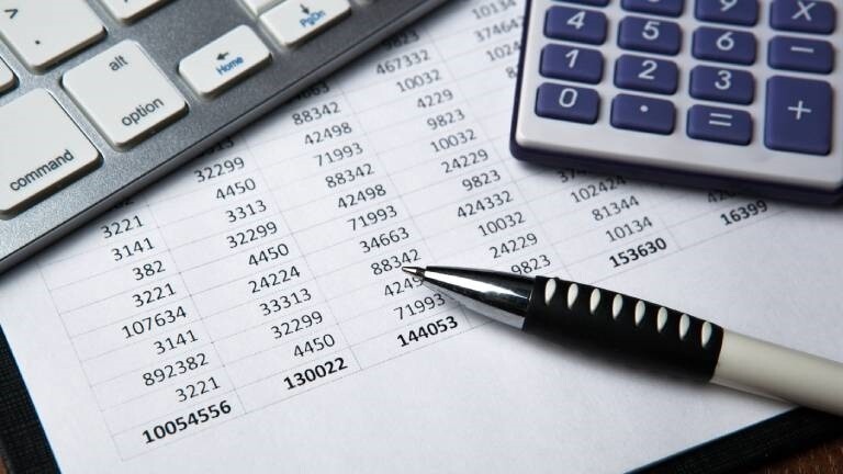 Eine ausgedruckte Excel-Tabelle unter einer Tastatur, einem Taschenrechner und einem Stift