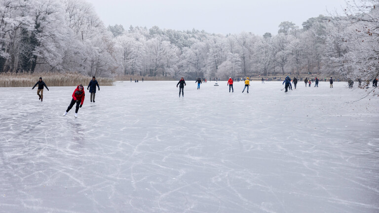 Auf einem gefrorenen See in Berlin sind einige Menschen mit Schlittschuhen unterwegs.
