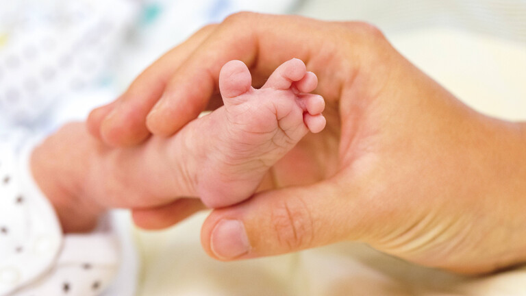 Eine Hand hält den Fuß eines Neugeborenen