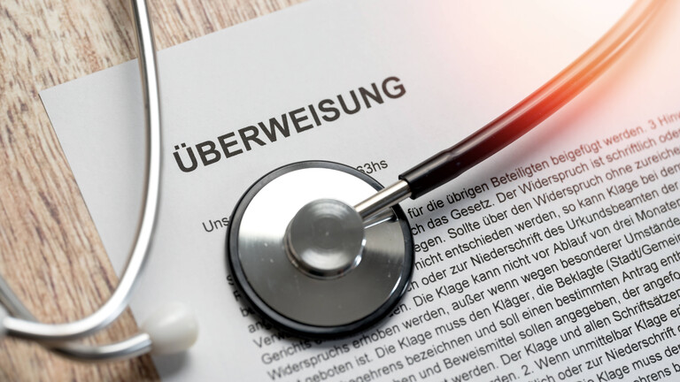 Ein Stethoskop liegt auf einem Dokument mit der Überschrift "Überweisung".