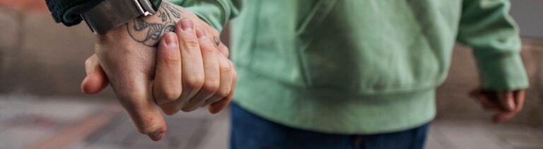 Zwei Männer halten Händchen. Das Paar läuft durch eine Straße. Wir sehen vor allem ihre Hände.