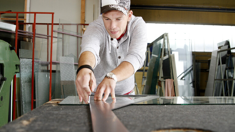Glasermeister Tobias Kinscher (24), der einen Spiegel mit Hilfe eines Hartmetallglasschneiders am Winkel schneidet.
