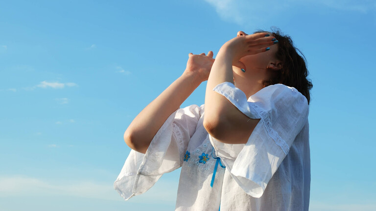 Eine Frau hält ihre Hände an den Mund und schreit in die Luft. Über ihr ist ein blauer Himmel.