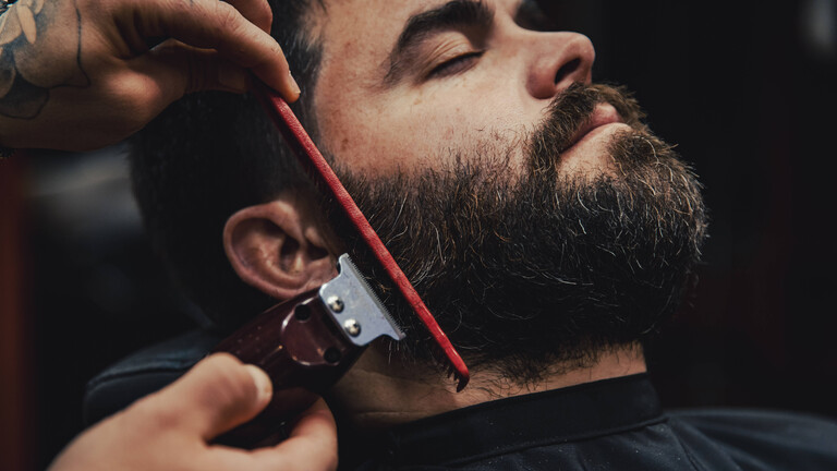 Foto eines Mannes, dem in einem Barbershop der Bart getrimmt wird
