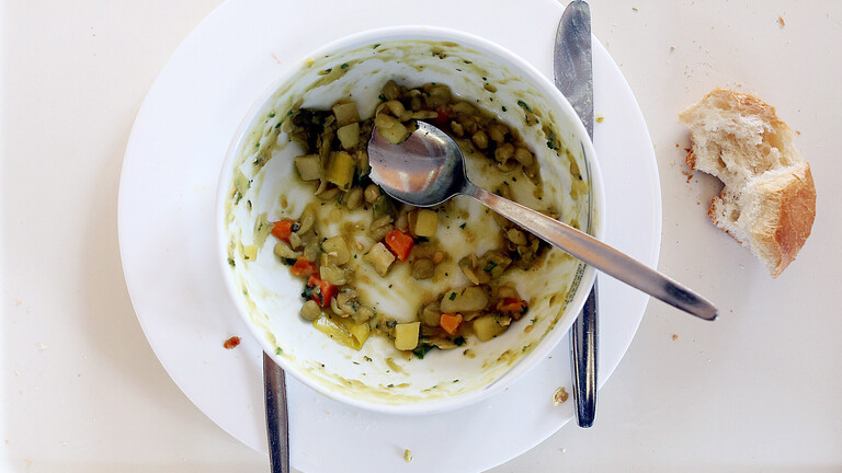 Auf einem Kantinentablett befindet sich eine Schüssel mit Eintopfresten, daneben ein halbaufgegessenes Brötchen.