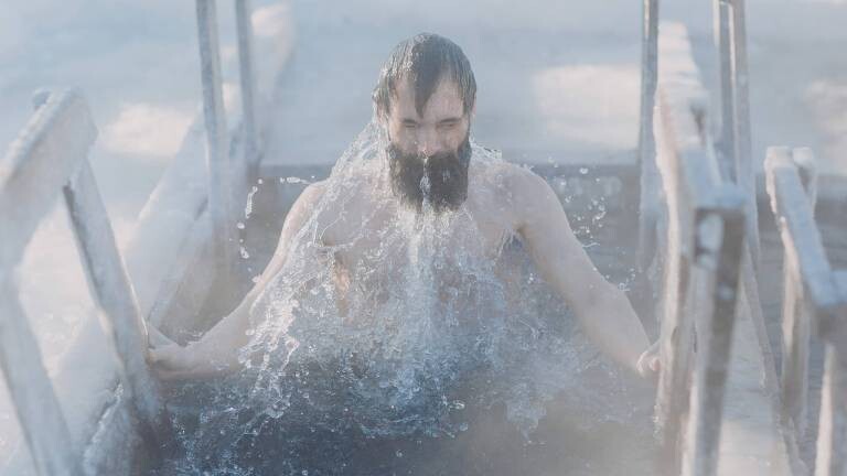 Person mit schwarzen Haaren und Bad taucht aus dem Eisbad auf
