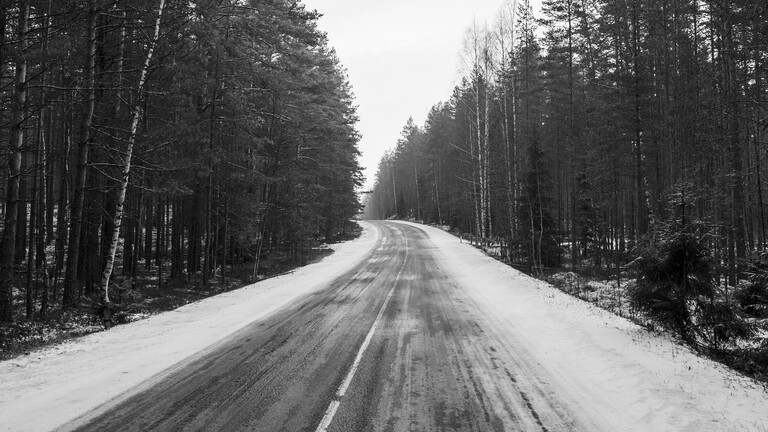 Eine verschneite Landstraße führt durch einen Wald.