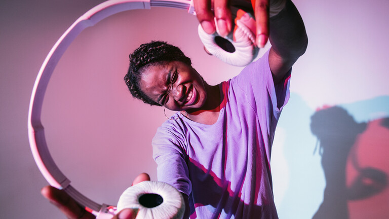 Eine Frau hält Kopfhörer in die Kamera.