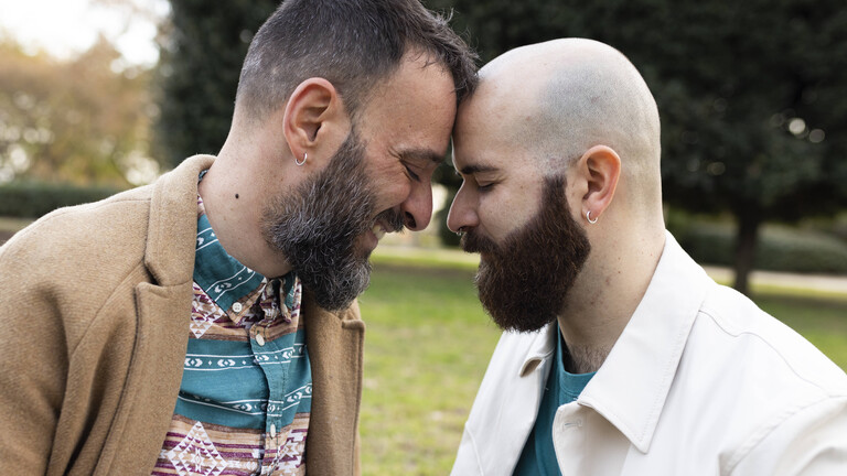 Zwei Männer lehnen ihre Köpfe liebevoll gegeneinander. Sie wirken vertraut.