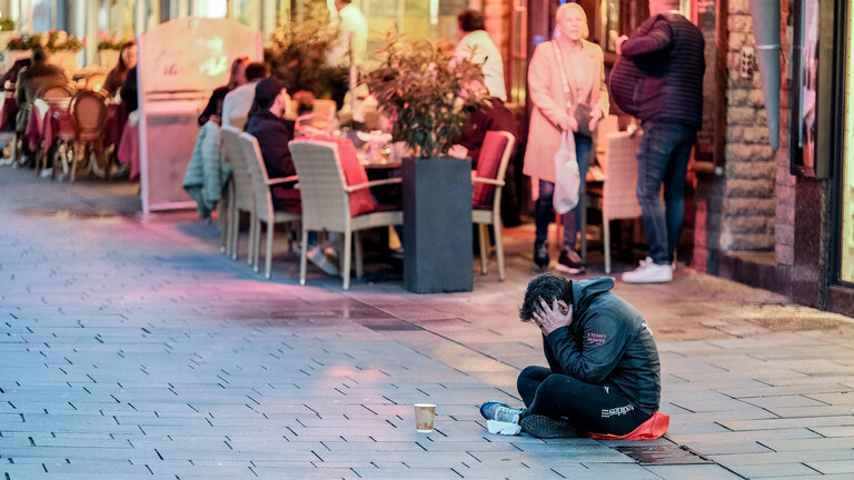 Ein Obdachloser sitzt in der Fußgängerzone, hinter ihm ein Café