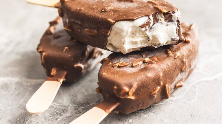 Drei Eis am Stil mit Schokoladenüberzug liegen aufeinandergestapelt auf einer Arbeitsplatte.