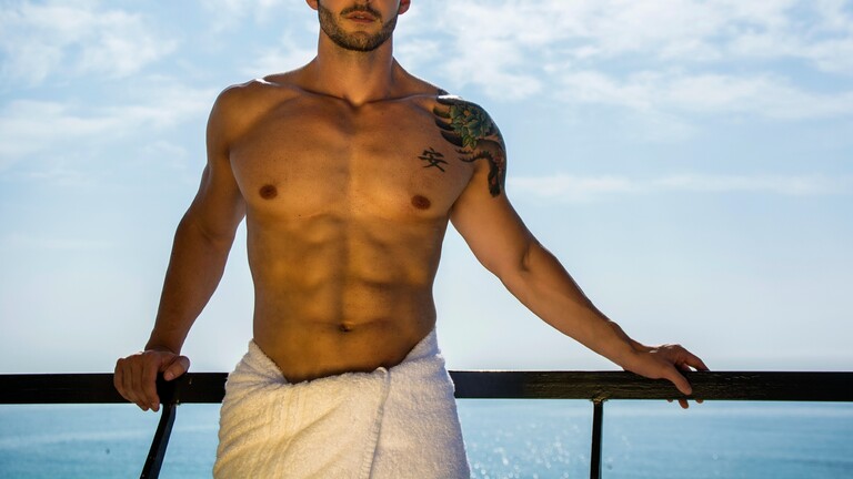 Ein Mann mit muskulösem, nackten Oberkörper lehnt an einer Reling.