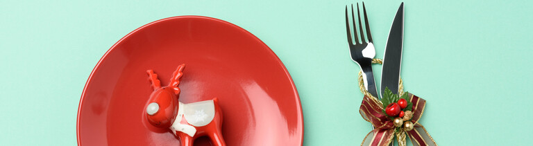 Ein roter Teller mit einem Elch und daneben Besteck mit Weihnachtsdekoration