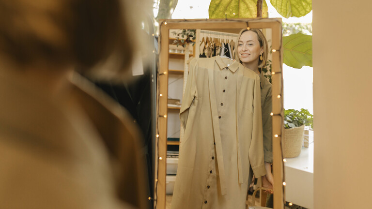 Eine Frau steht vor einem Spiegel und hält ein Kleid vor sich.