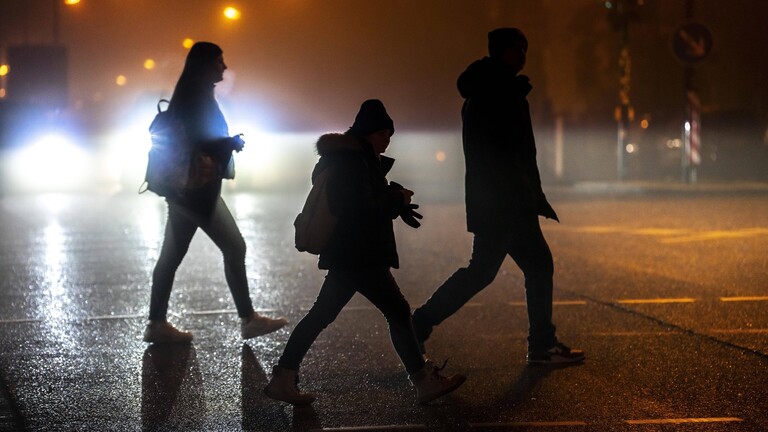 Fußgänger üerqueren eine Straße im Dunkeln.